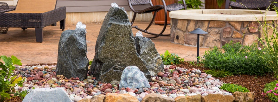A bubbling rock water feature installed next to a new paver patio and fire pit at a home in Fort Collins.