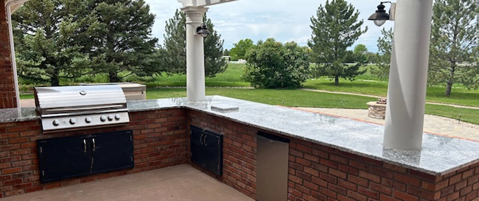 Outdoor kitchen with a grill and bar in the backyard of a property in Fort Collins, CO.